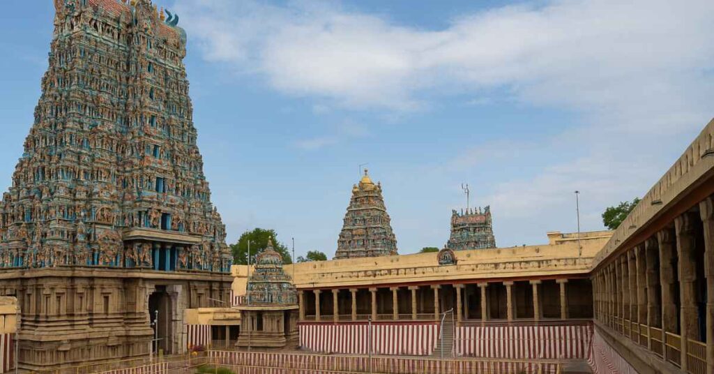 Meenakshi Amman Temple Vibrant view of Meenakshi Amman Temple Madurai showing the gopuram towers, temple tank, and Dravidian sculptures under a bright blue sky.